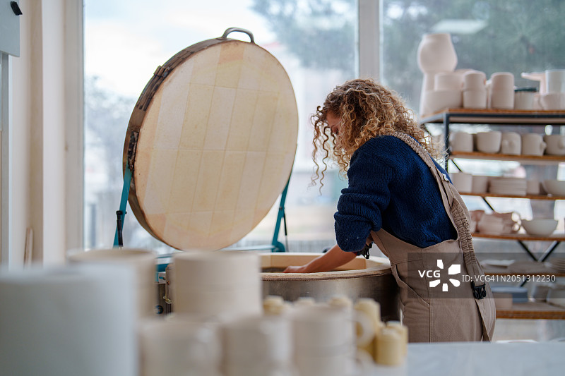 女人从陶瓷窑中取出陶瓷罐图片素材