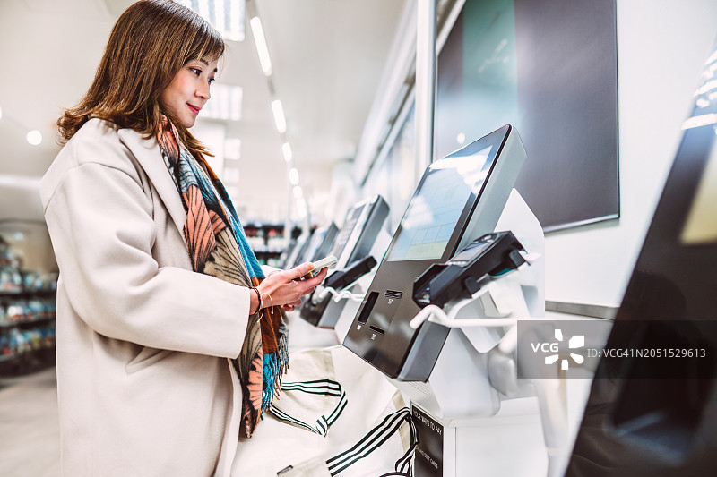 漂亮的亚洲女人在超市自助结账时使用智能手机进行非接触式支付图片素材