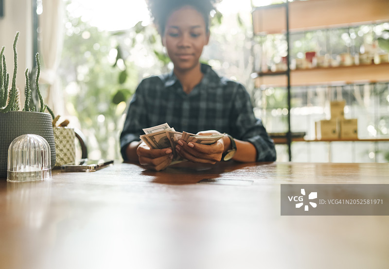 小咖啡馆的年轻非裔混血店主用手清点美元钞票图片素材