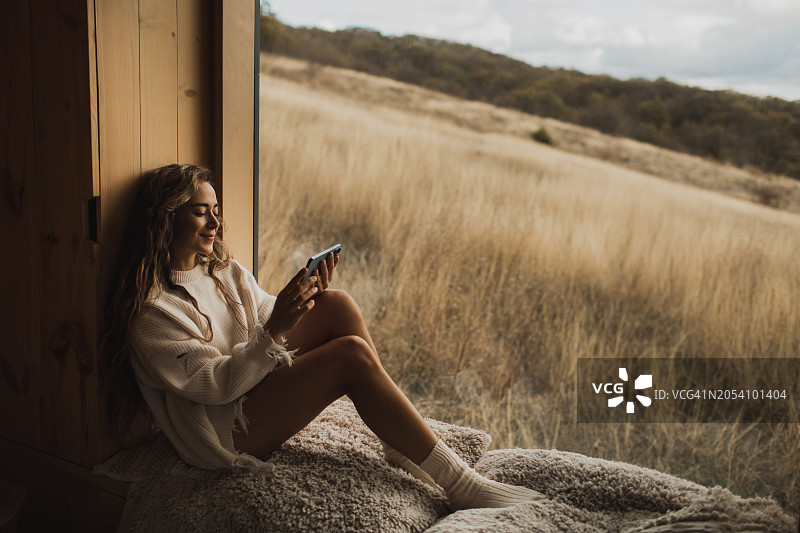 女人在小屋的窗台上放松，用手机消磨时间，在线看电影图片素材