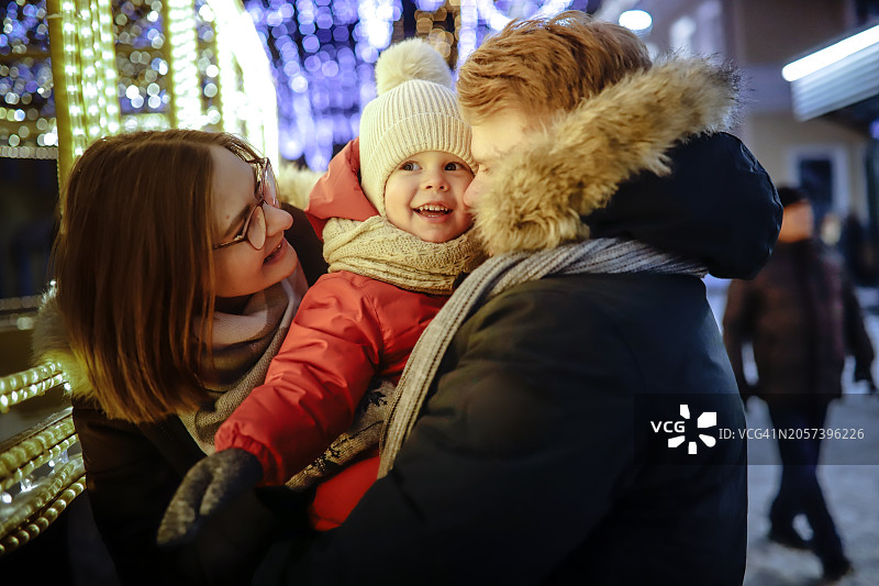 节日气氛：幼儿与家人在冬季服装中于户外摆姿势，城市灯光图片素材