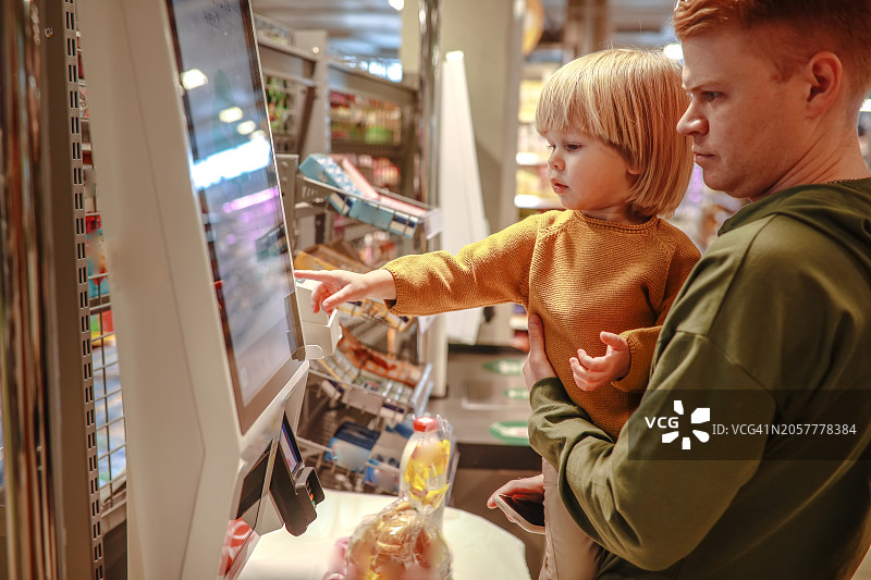 父子购物：在自助收银机使用智能手机付款图片素材