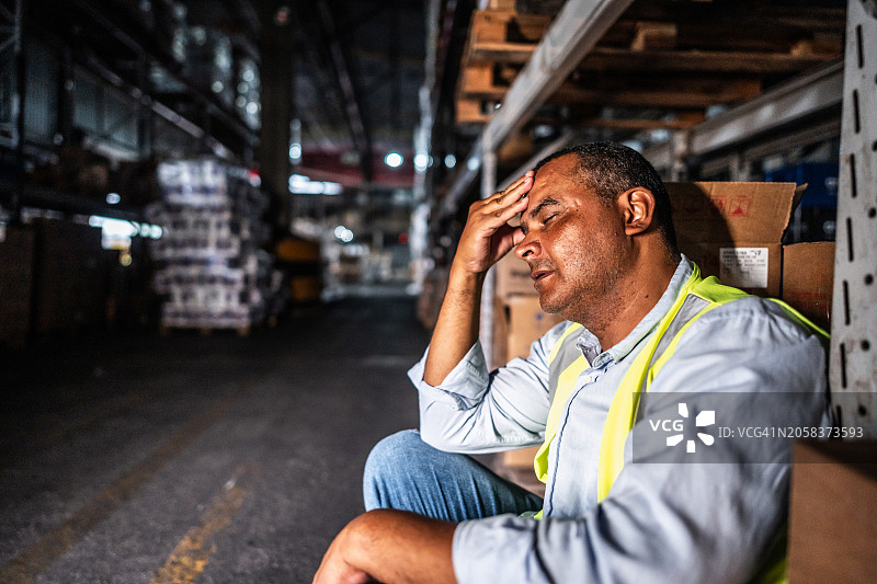 疲惫的中年男人坐在仓库里工作图片素材