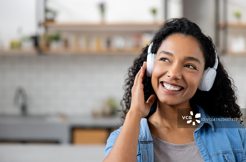 快乐的女人在家戴着耳机听音乐，面带微笑图片素材