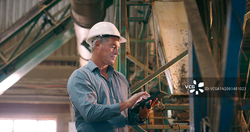 戴着头盔的成熟男子使用平板电脑进行工程、工业和检查，使用在线软件或互联网。建筑师和员工使用科技或数字应用程序，注意施工安全图片素材