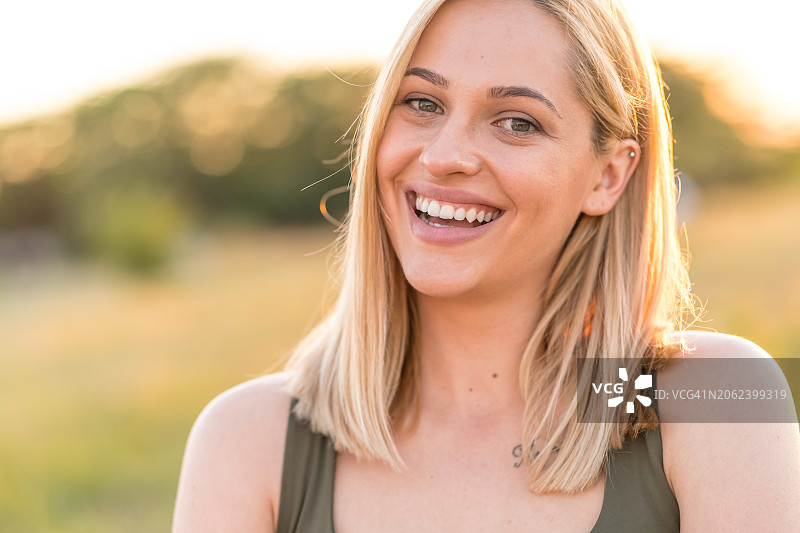 美丽的金色女人在日落时分看着草地前的相机图片素材