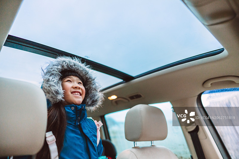 在雨天里，穿着连帽外套的可爱女孩在车里放松身心，透过天窗向外看图片素材