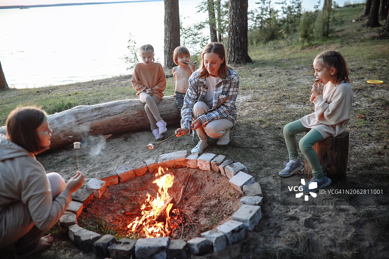 母亲和四个孩子在森林的河边烤棉花糖图片素材