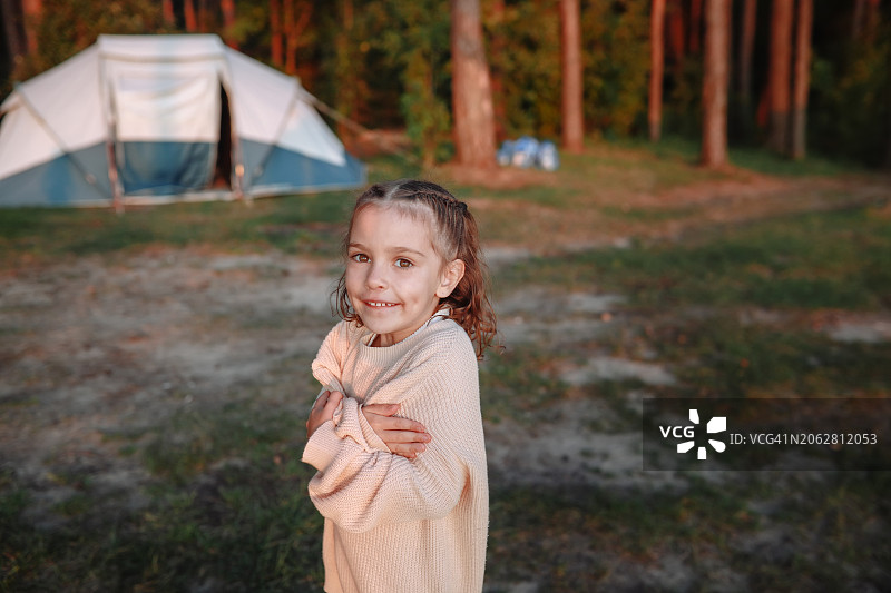 在露营地，穿着毛衣的小女孩拥抱自己取暖图片素材