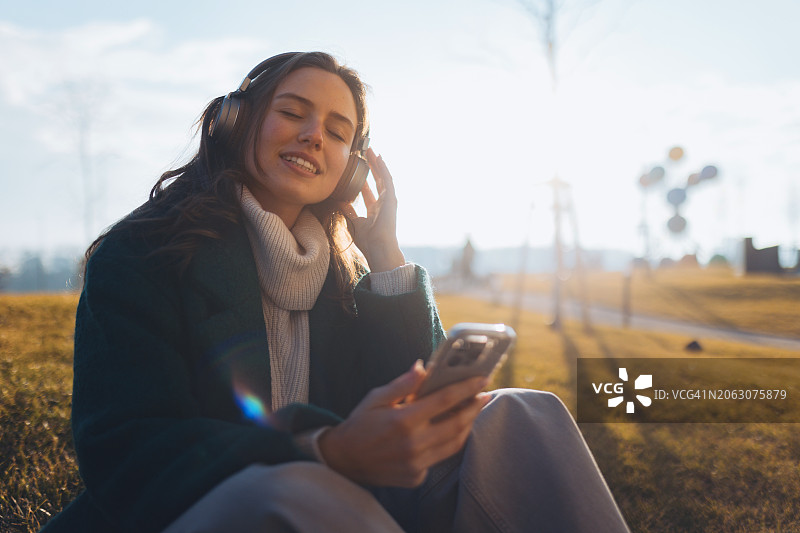 听着音乐，坐在草地上的年轻漂亮女人图片素材