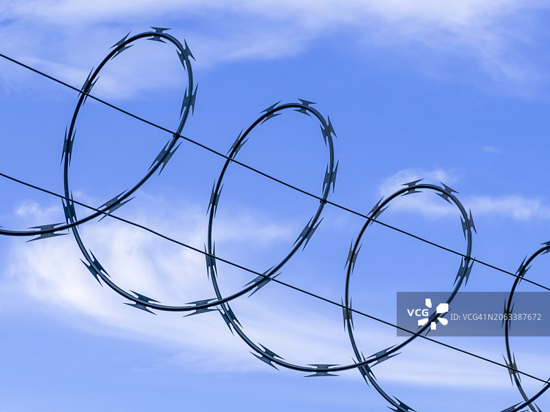 蓝天下带刺铁丝网的金属栅栏细节图片素材