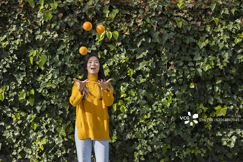 在植物前玩橙子的快乐年轻女人图片素材