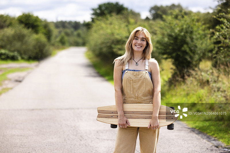 手持滑板在路上微笑的年轻女人图片素材