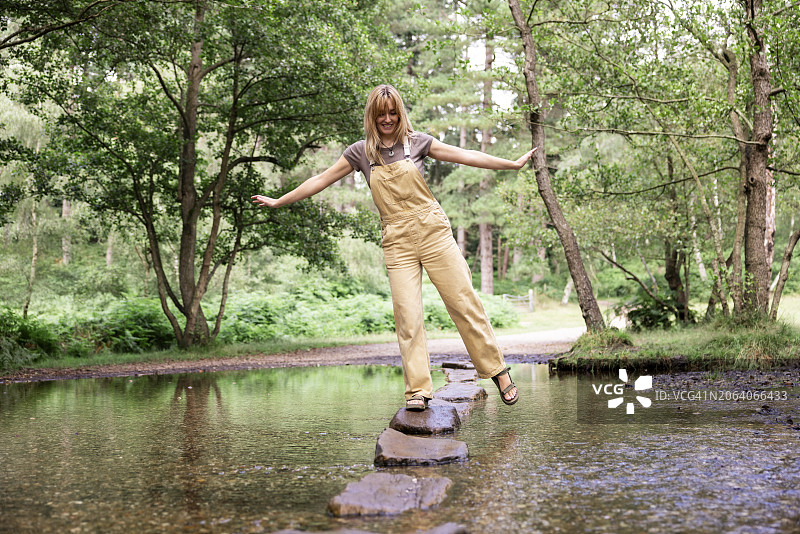 快乐的年轻女人在河里的岩石上保持平衡图片素材