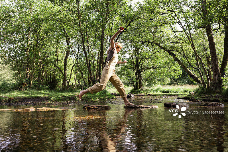 女子在河水中岩石上跳跃图片素材
