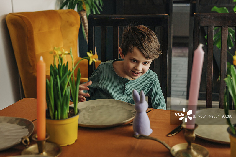 微笑的男孩在餐桌旁看着复活节兔子图片素材
