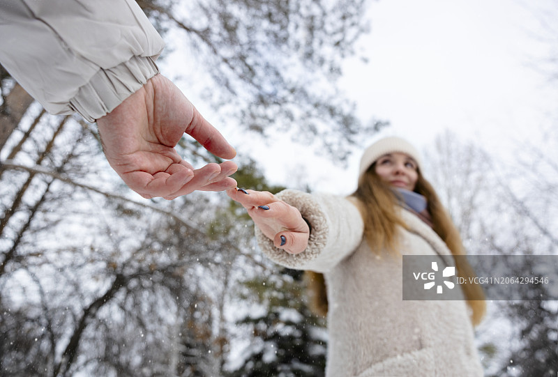在冬季公园里，年轻女人伸手去牵男人的手图片素材