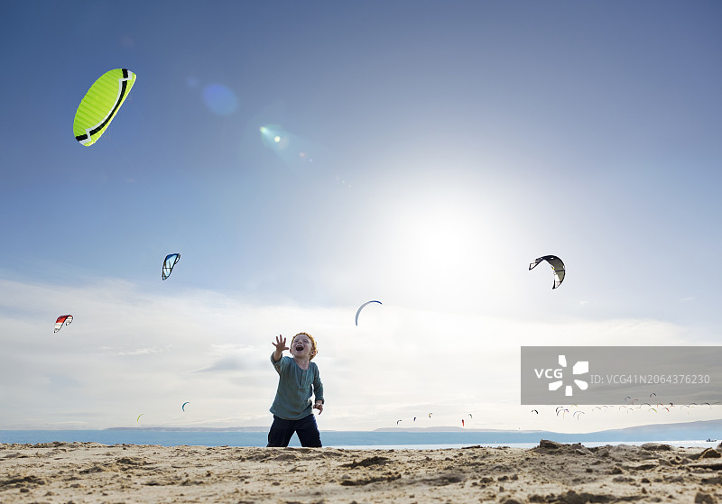快乐的男孩在阳光明媚的海滩上观看风筝冲浪者图片素材
