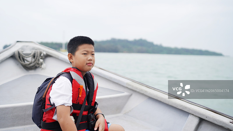 在海中央坐在快艇上的穿救生衣的年轻亚洲男孩图片素材
