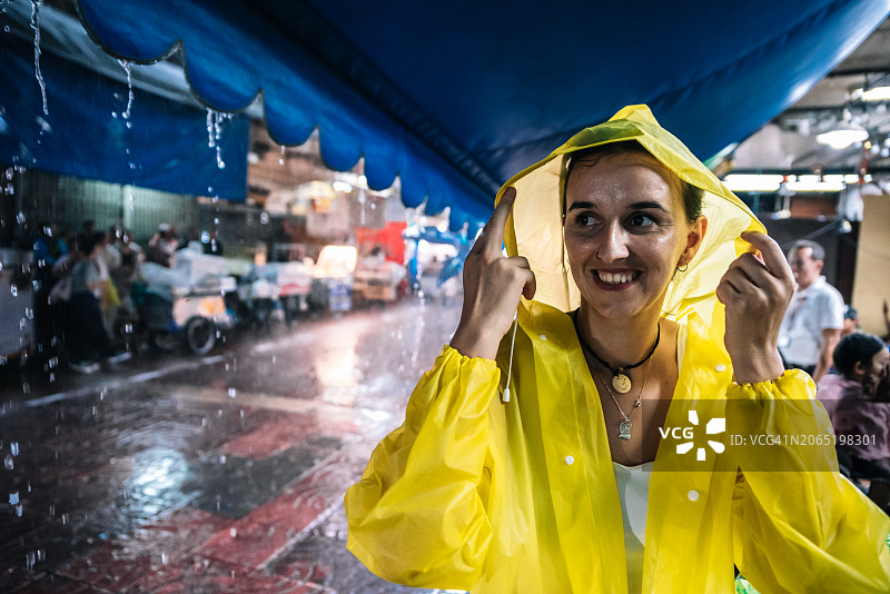 在曼谷的雨夜，年轻女子用雨衣的兜帽遮住自己图片素材