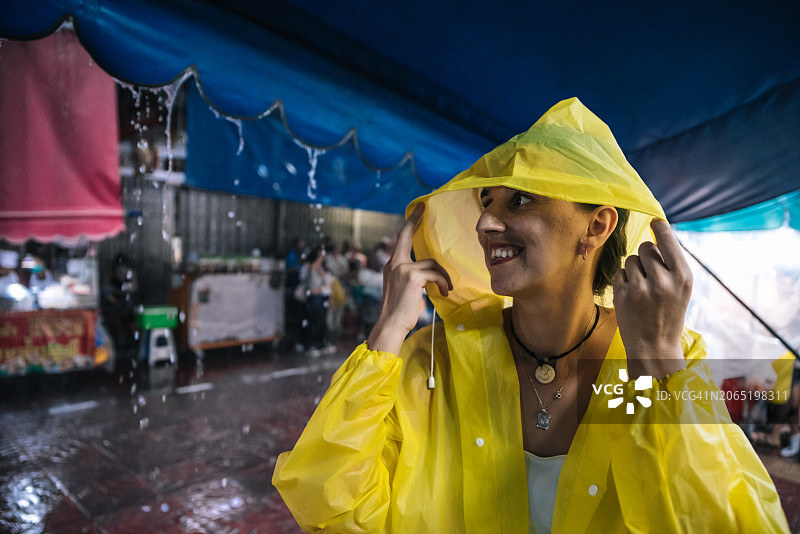 在曼谷的雨夜，年轻女子用雨衣的兜帽遮住自己图片素材