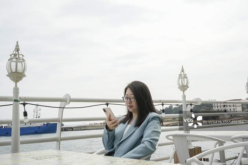 女人坐在海景餐厅里，用手机工作图片素材