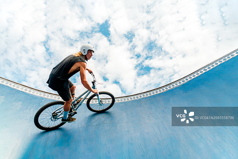大胆的中年男子在滑板公园边缘骑自行车，天空布满明亮的云彩图片素材
