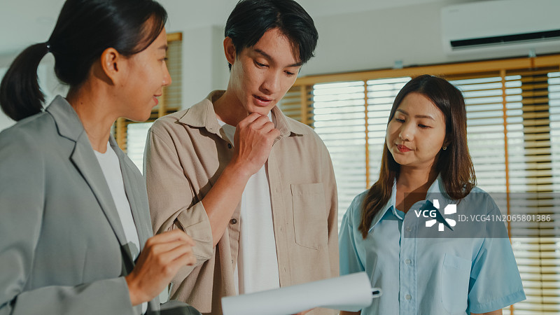 亚洲女房地产经纪人向租户解释并展示新房客厅，房东向幸福的夫妇客户出售房地产图片素材