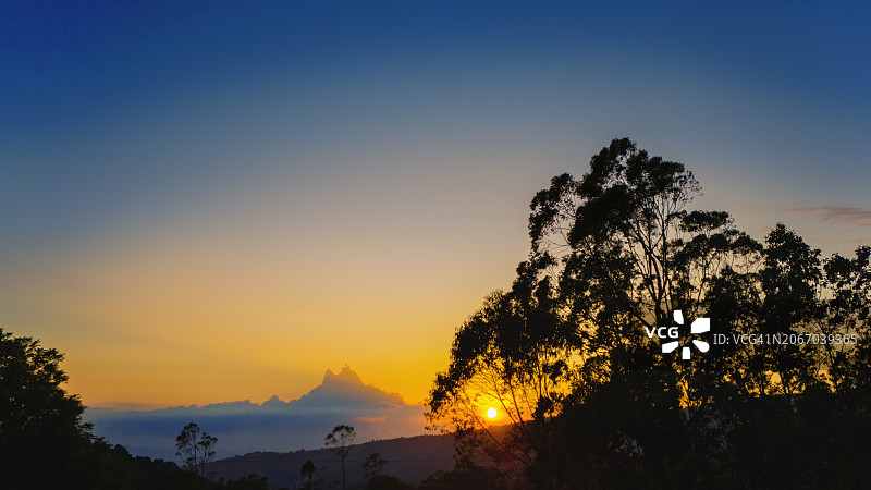 日落时分暖色天空和红色太阳下的树木轮廓图片素材