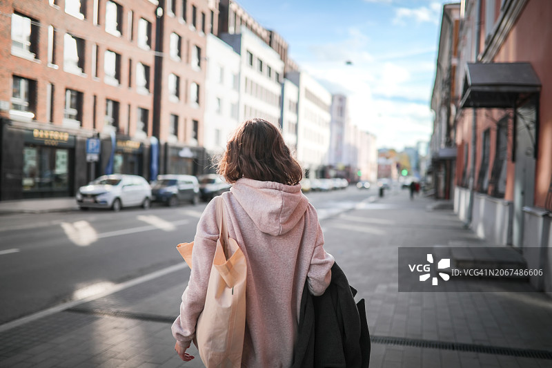积极的生活方式：身穿运动服的中年女士提着包在城市中步行。后视图图片素材