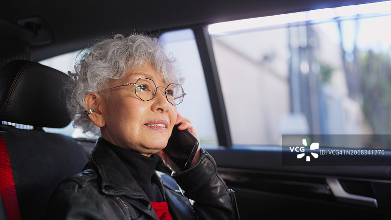 亚洲老年女商人开车通勤时用手机图片素材