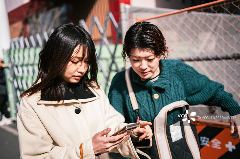 年轻的日本女性在街上看手机上的位置。图片素材