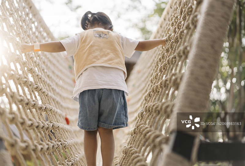 快乐瞬间：亚洲年轻儿童自信地张开双臂过绳桥图片素材