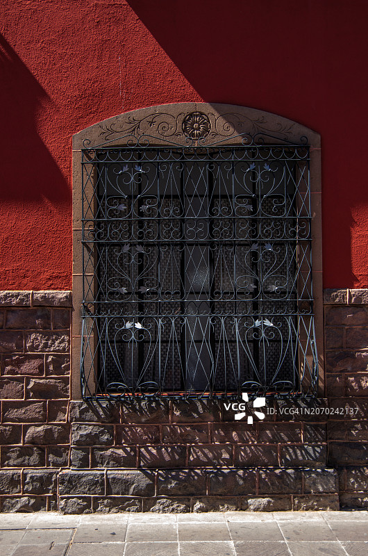 殖民时期房屋的窗户，窗户上有人工铁栅栏，雕刻的石框装饰和红色粉刷墙图片素材
