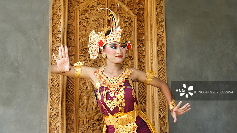 巴厘岛女孩舞蹈演员，身穿巴厘岛传统服饰，背景是雕刻有巴厘岛图案的门图片素材