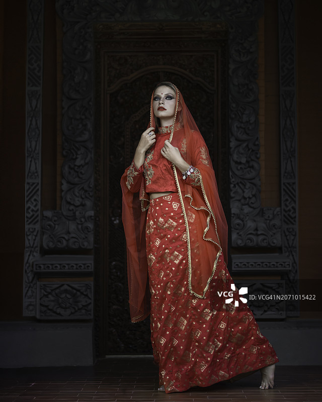 身穿印度红色服装的女孩站在雕刻墙前图片素材