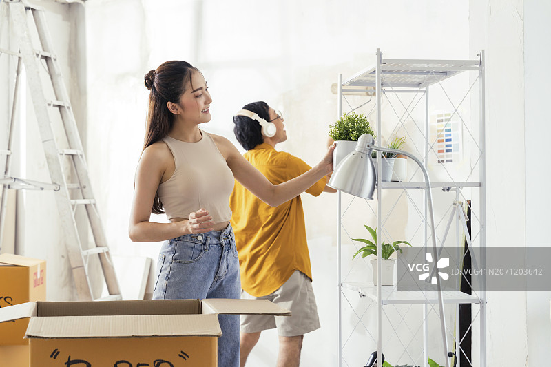 亚裔夫妇一起重新装修房屋，妻子整理物品，丈夫粉刷墙壁图片素材