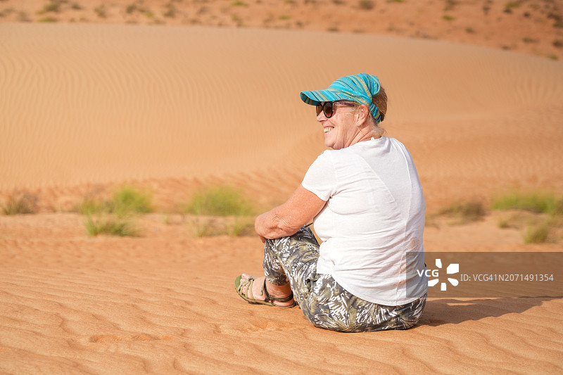 年长的女人坐在阿曼瓦希巴沙漠的沙滩上图片素材
