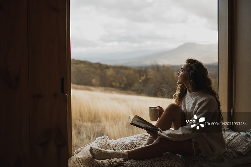 女人在窗台上读书喝茶，享受秋日居家舒适图片素材