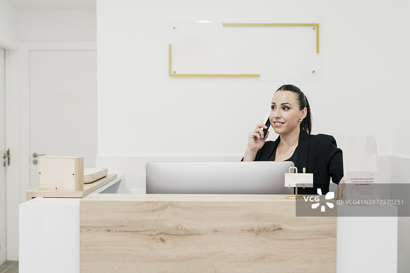 一个人在现代优雅的办公室里，站在浅色木质柜台后打电话图片素材