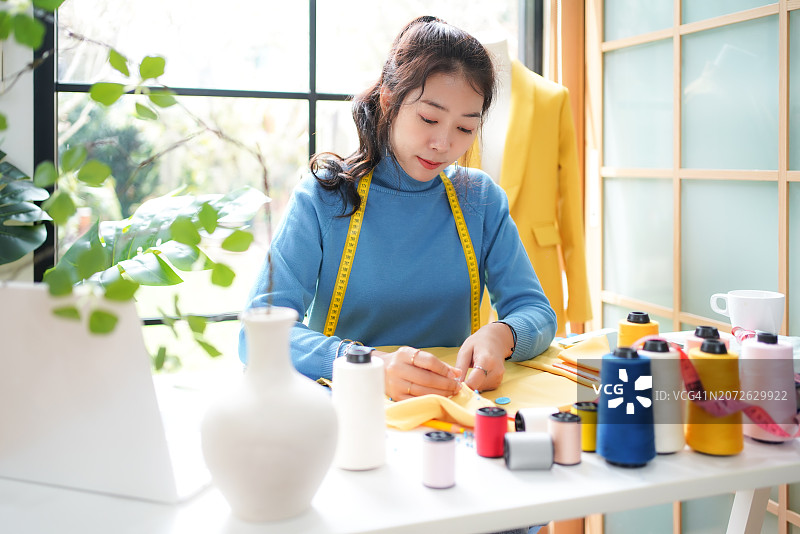 亚洲女装设计师在展厅设计服装，时尚裁缝在工作室裁剪布料。小型商业概念图片素材