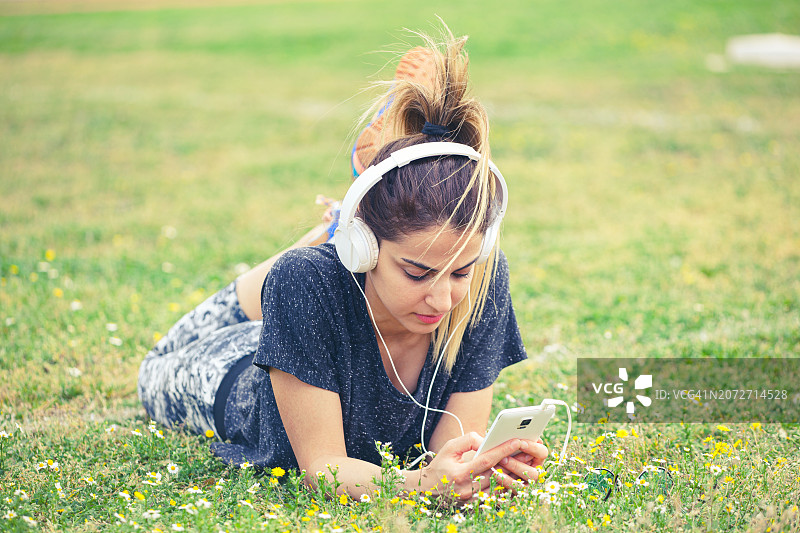 在公园绿草地上戴着耳机的年轻运动女性图片素材