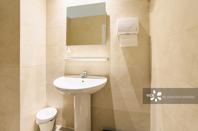 浴室一角：水槽、镜子、纸巾、热水器和塑料垃圾桶图片素材