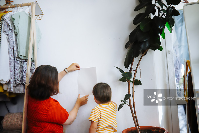 中年加大码母亲和幼儿儿子一起在墙上的纸上贴上模拟图图片素材