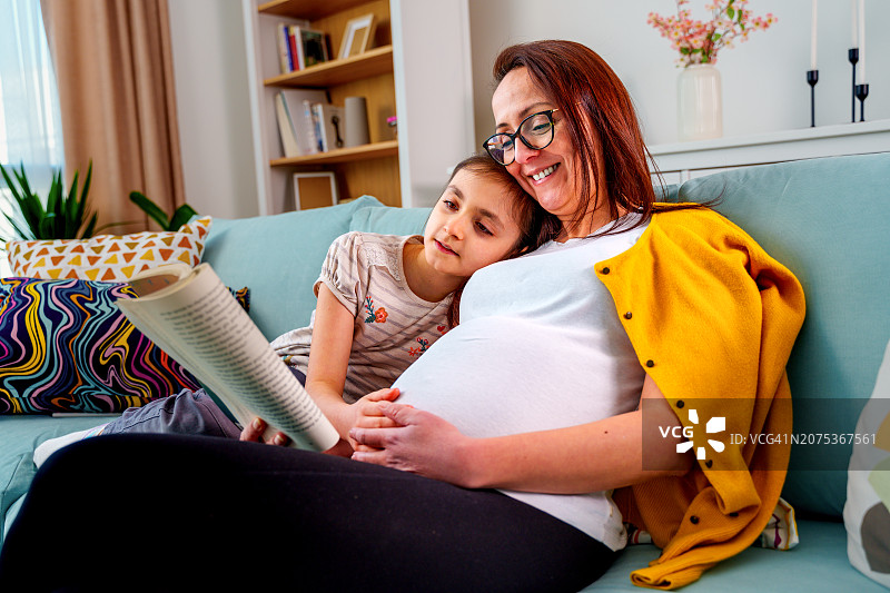 怀孕的母亲和女儿在家读书图片素材