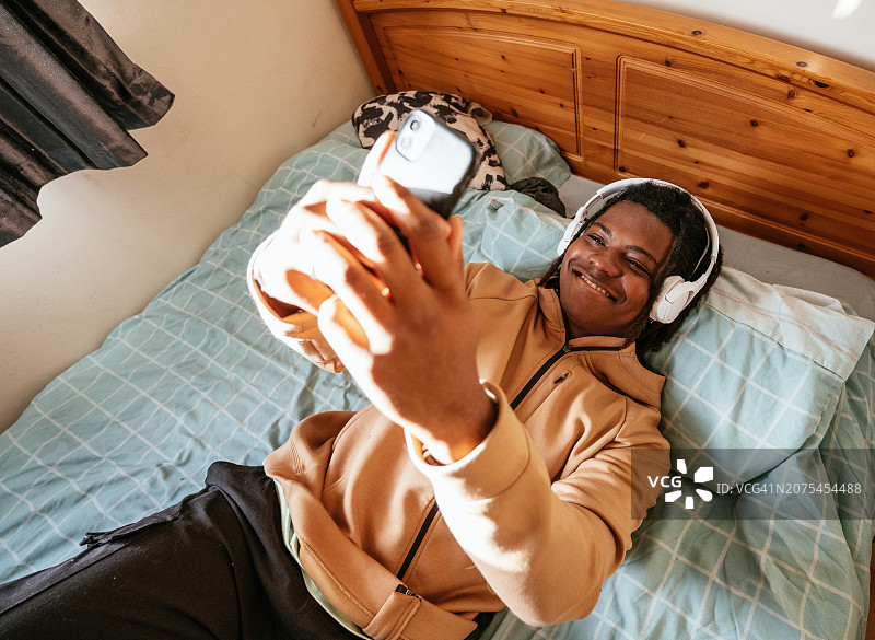 在卧室里使用智能手机和无线耳机的青少年图片素材