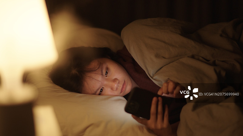 晚上在床上使用智能手机的女孩图片素材