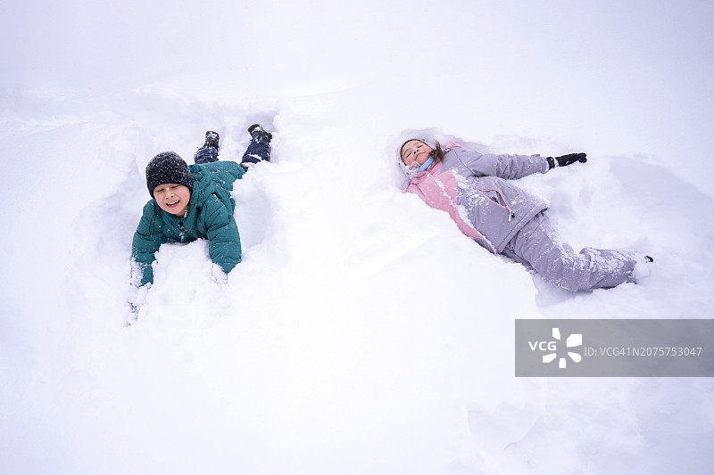 兄妹俩带着调皮的笑容躺在蓬松的白雪中手牵着手图片素材