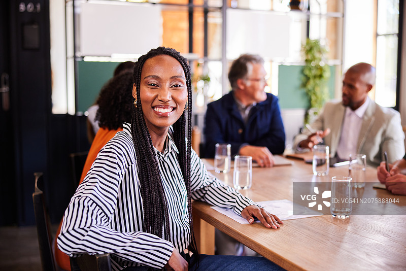 年轻女商人在会议室微笑，同事在背景中图片素材