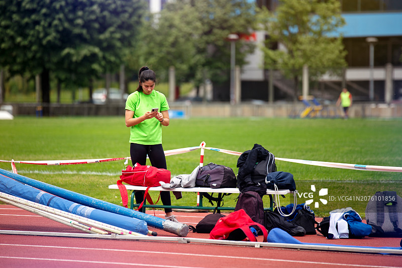 在跑道上使用智能手机的年轻女运动员图片素材